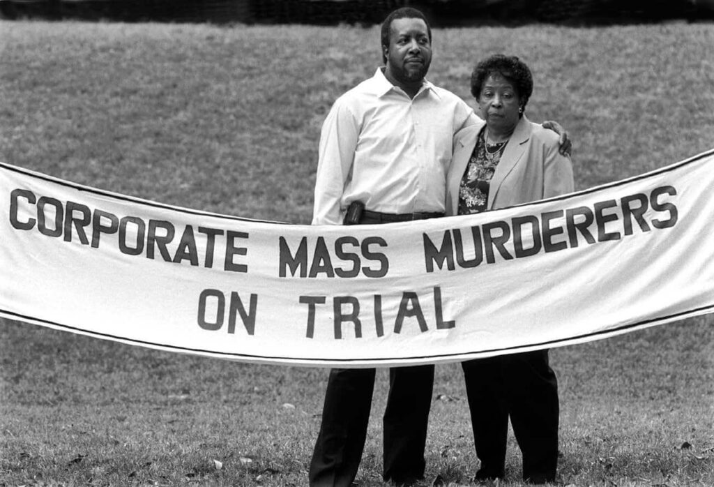 couple protesting with sign "corporate mass murderers on trial"